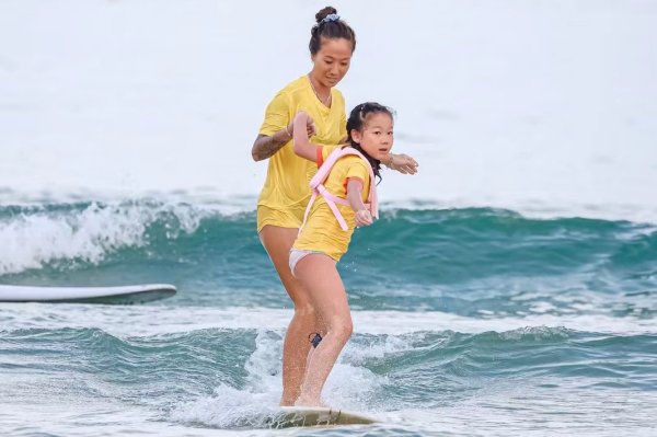 青少年兒童在沖浪教練的陪同下，在三亞市海棠區(qū)夏日水上運(yùn)動嘉年華灣“乘風(fēng)破浪”。三亞市體育旅游協(xié)會供圖